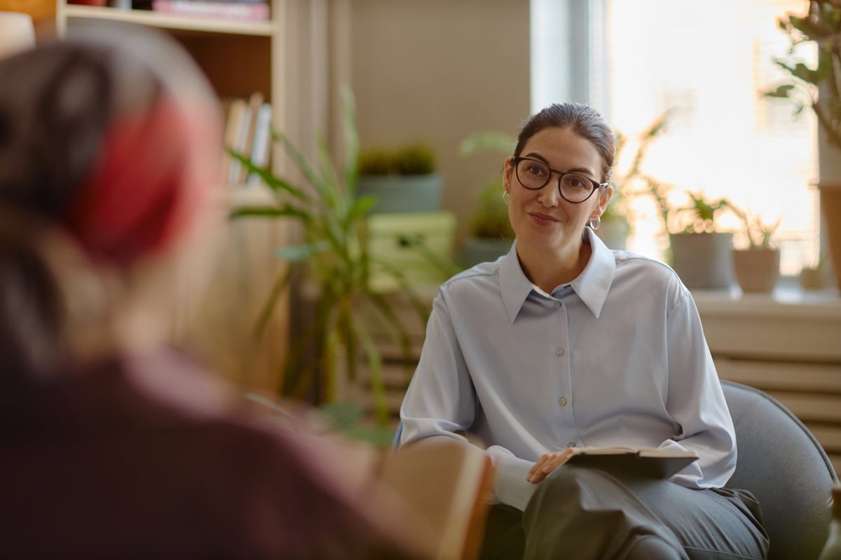 Young adult woman psychologist wearing glasses listening attentively to patient during therapy session.